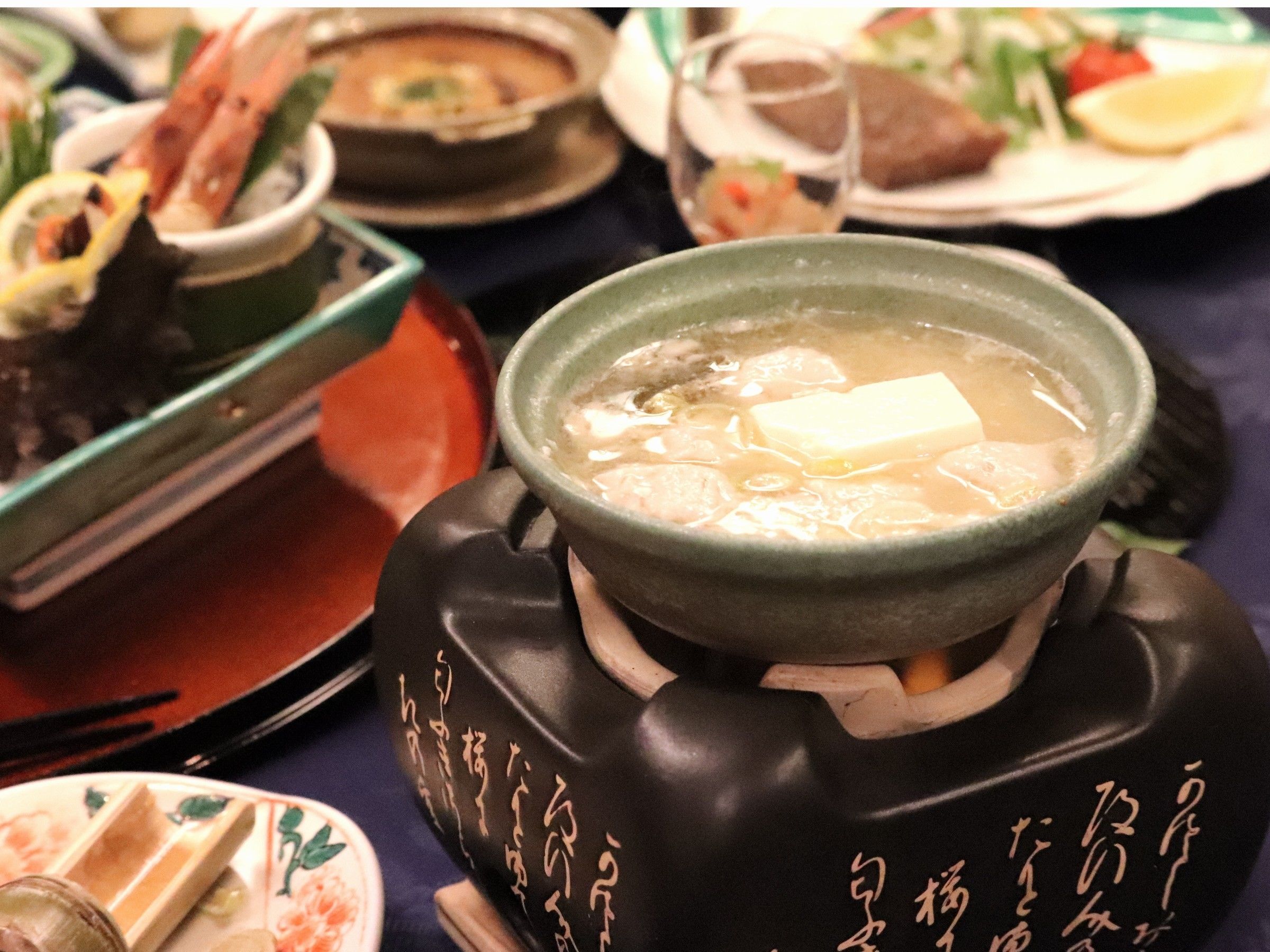 A traditional Japanese hot pot with tofu and vegetables, surrounded by various dishes on a table.