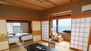 Une pièce de style japonais traditionnel, avec un sol recouvert de tatamis, une table basse en tatami, un futon servant de lit, un fauteuil rembourré et une vue sur la mer, visible à travers une porte coulissante.