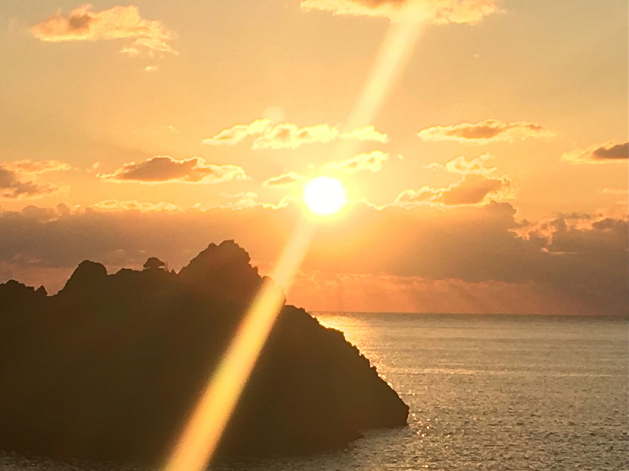 Un atardecer sobre un paisaje costero con una formación rocosa destacada silueteada contra el cielo.
