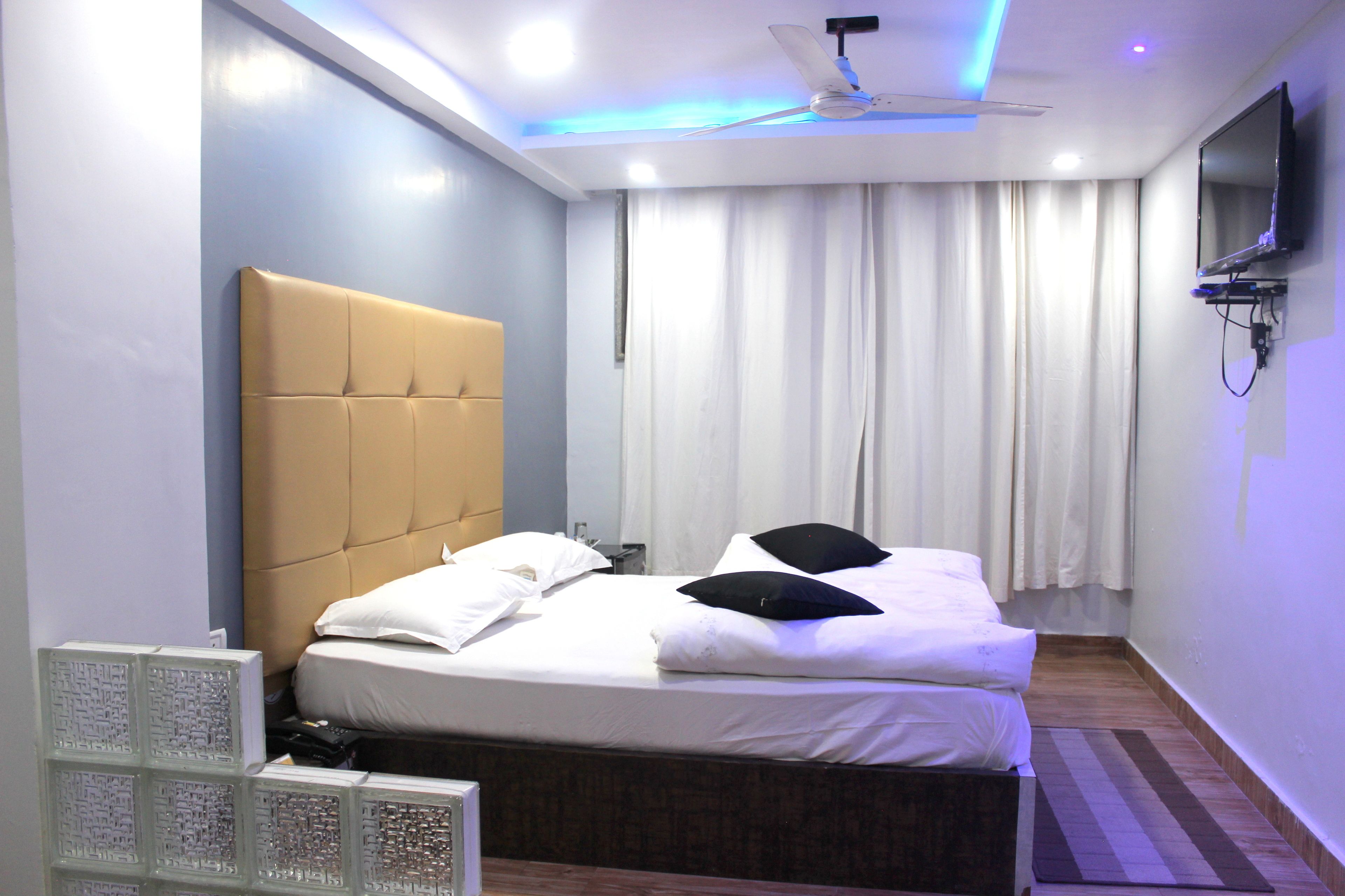A bedroom with a bed, a ceiling fan, a TV, and a window with curtains.