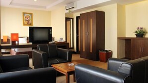 Habitación de hotel con zona de estar, televisor, mueble y un cuadro en la pared.