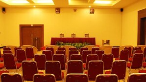 Un salón de conferencias con filas de sillas rojas, un atril y un telón de fondo rojo.
