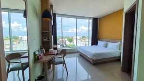 Ein Hotelzimmer mit Bett, Schreibtisch, Stuhl, einem großen Fenster und Blick auf die Stadt.