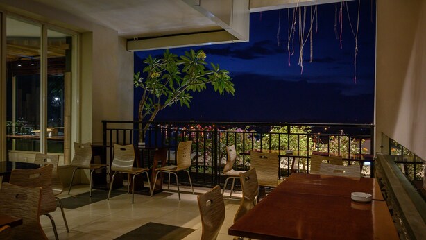 Ein Restaurant mit Blick auf den Nachthimmel, ausgestattet mit einem großen Tisch, Stühlen, einem Blumentopf und einem Balkon mit Geländer.