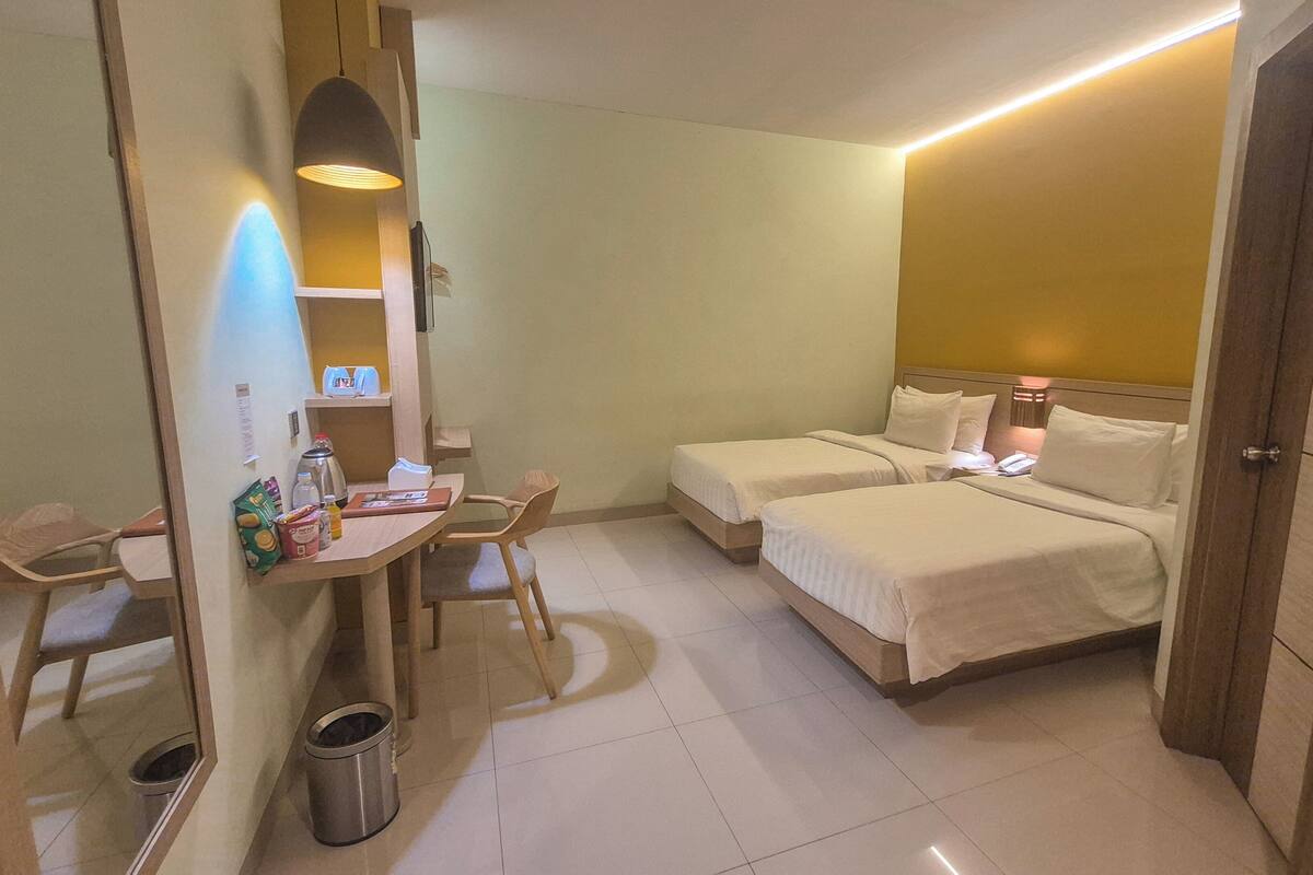 A hotel room with two beds, a small desk with a chair, a trash bin, and a mirror.