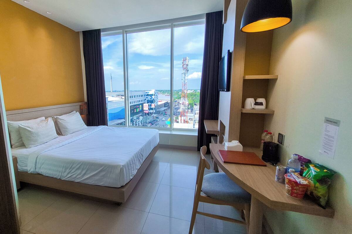 A hotel room with a bed, a desk, a chair, a TV, and a view of the city.