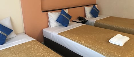Una habitación de hotel con tres camas, cada una con una colcha estampada y almohadas azules.