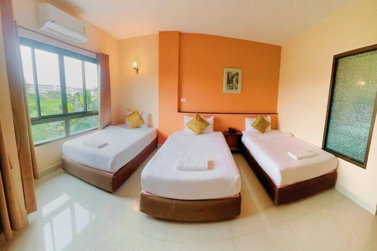 Une chambre d’hôtel avec deux lits simples, une grande fenêtre, un appareil de climatisation et un tableau encadré au mur.