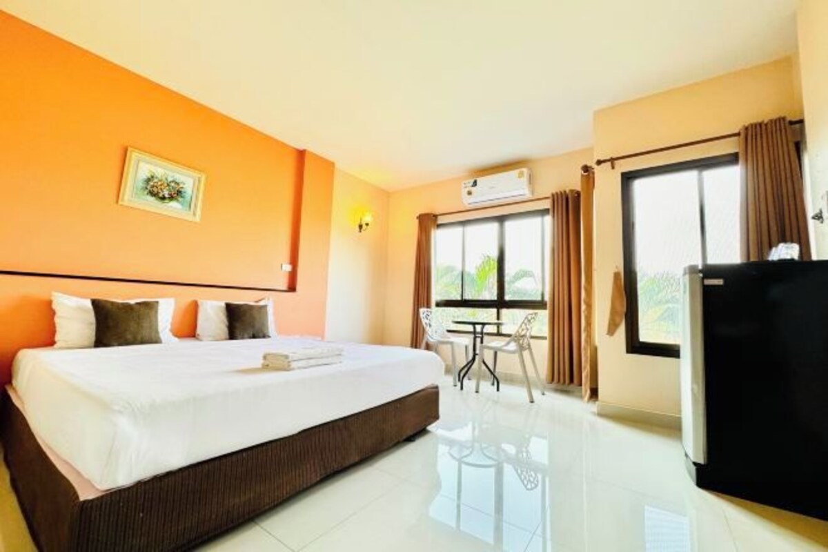 Habitación de hotel con cama, escritorio, silla, refrigerador y ventana con cortinas.