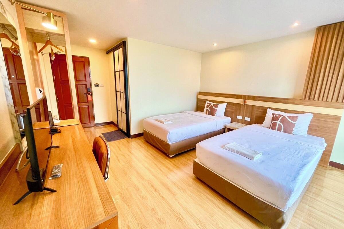 Une chambre d’hôtel avec deux lits, un bureau avec un ordinateur, un miroir et une armoire.