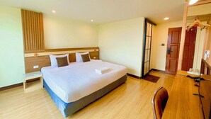 Una habitación de hotel con una cama grande, mesitas de noche, un armario, un escritorio y un espejo.
