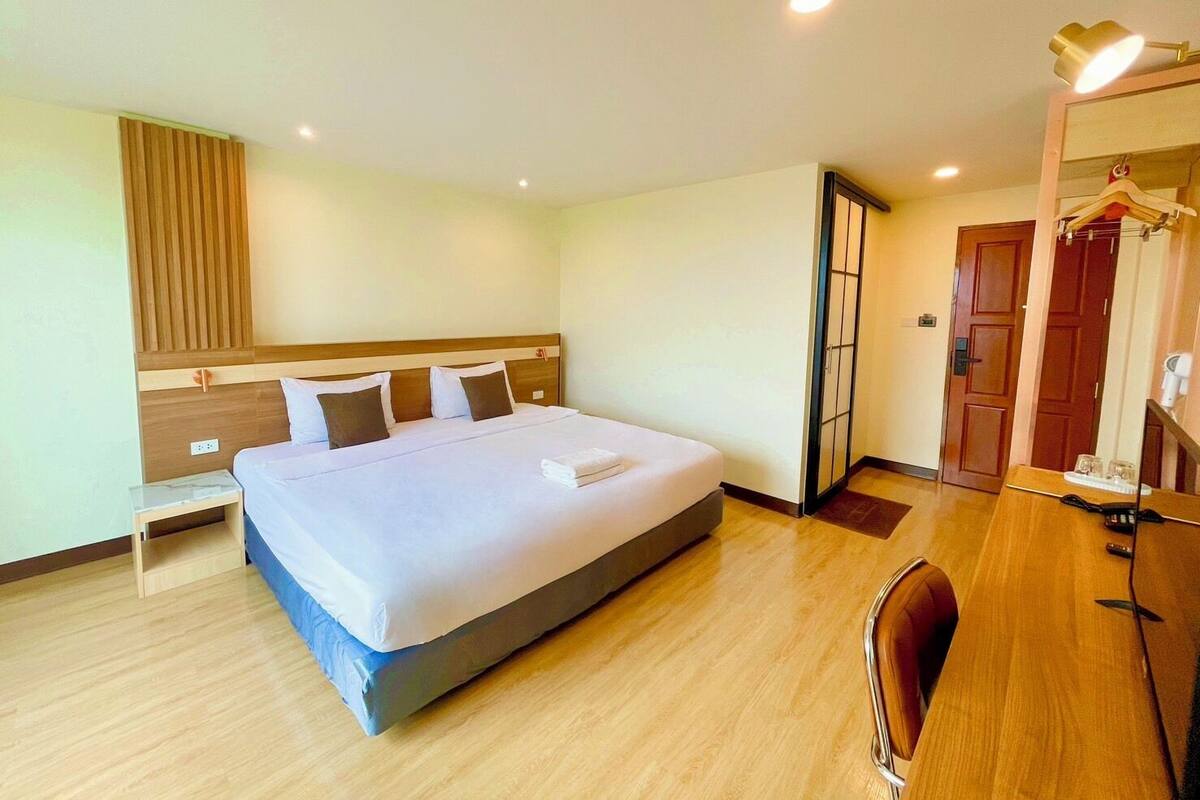 Une chambre d’hôtel avec un grand lit, des tables de chevet, une armoire, un bureau et un miroir.