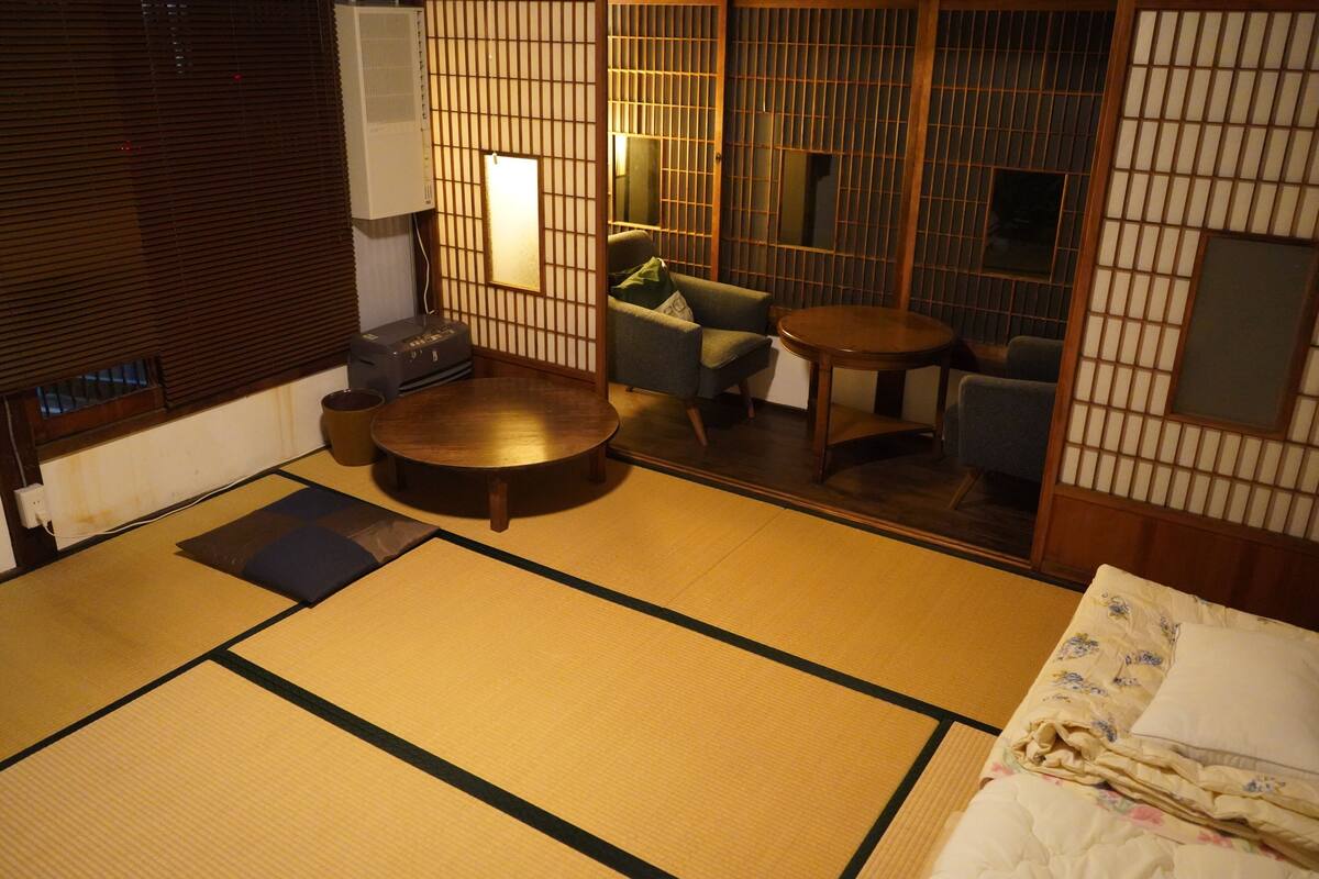 A tatami mat room with a futon bed, a round table, and a low wooden cabinet.
