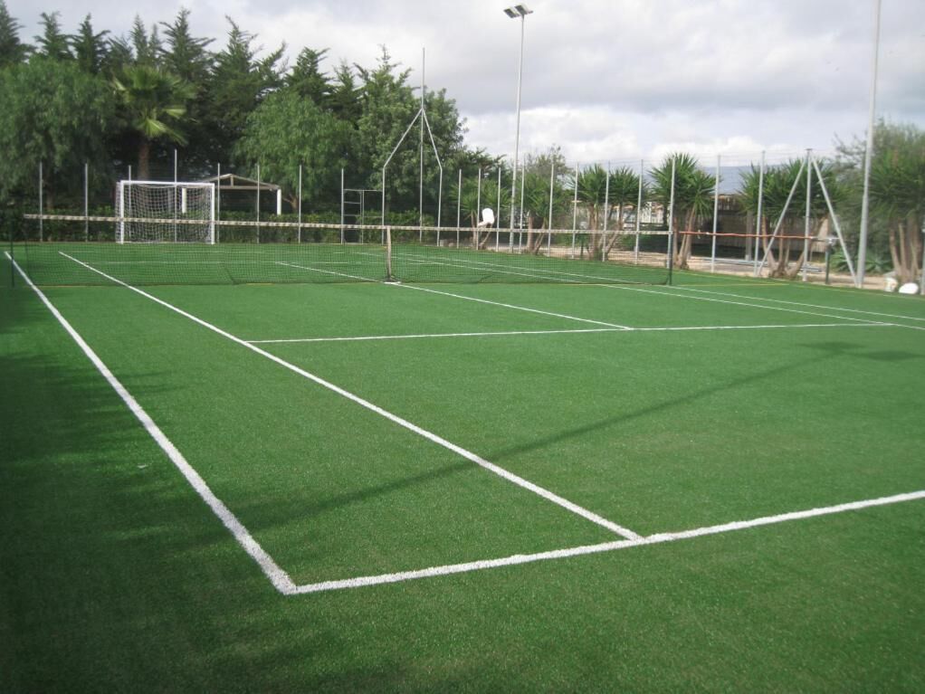 A tennis court with a net, surrounded by trees and a goalpost.