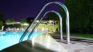 A swimming pool with metal railings, lounge chairs, and umbrellas in the background. - L'Araucaria (Santa Croce Camerina)