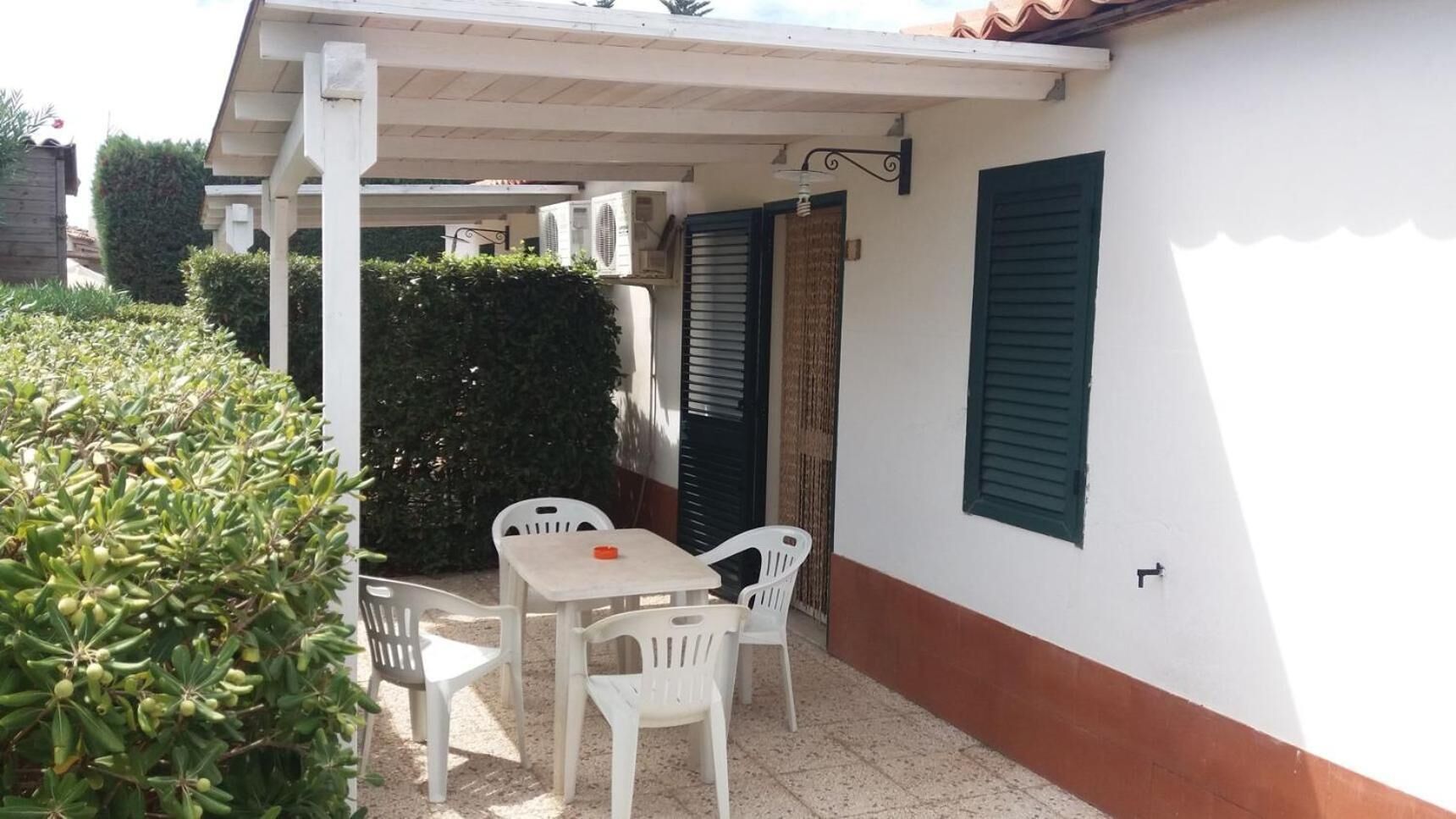 A patio with a table and chairs, a covered area, and a wall with shutters.