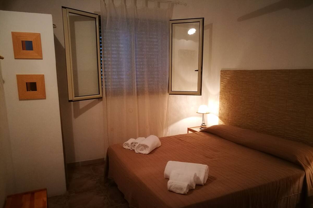A hotel room with a bed, a nightstand with a lamp, and two wall-mounted mirrors.
