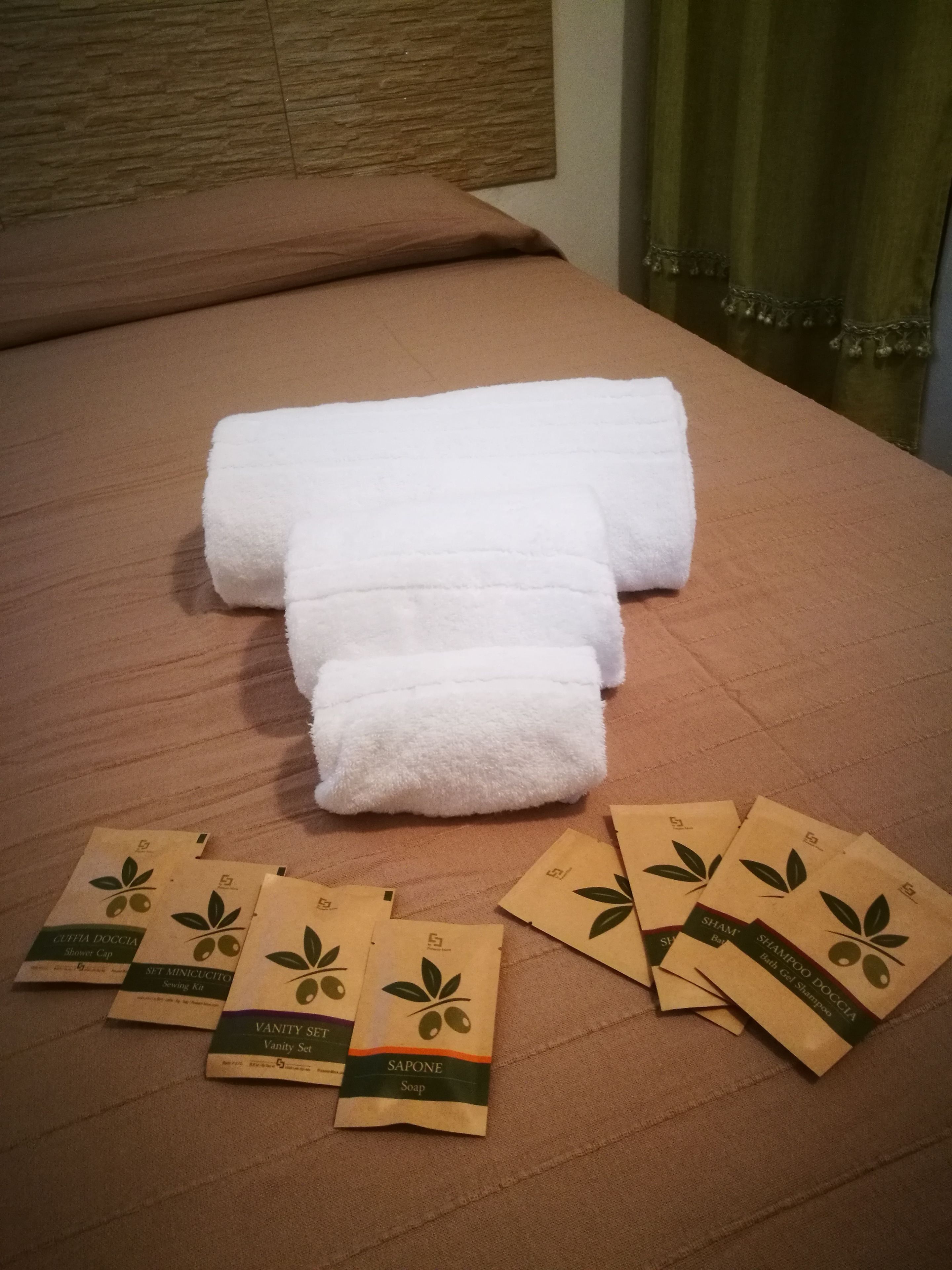 Un lit bien fait, avec une serviette blanche et plusieurs sacs en papier brun étiquetés avec le nom de produits de spa.