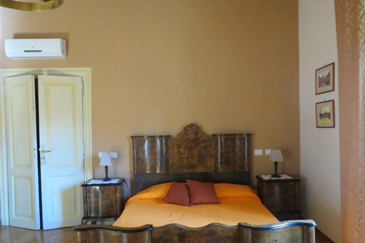 A bedroom with a wooden bed, two bedside tables, a white door, and a wall-mounted air conditioner.