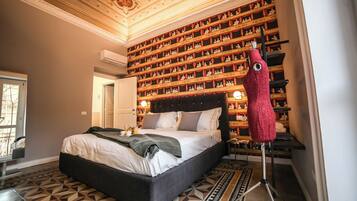 Un dormitorio con una cama grande, un suelo estampado, una estantería con figuritas y una silla roja.