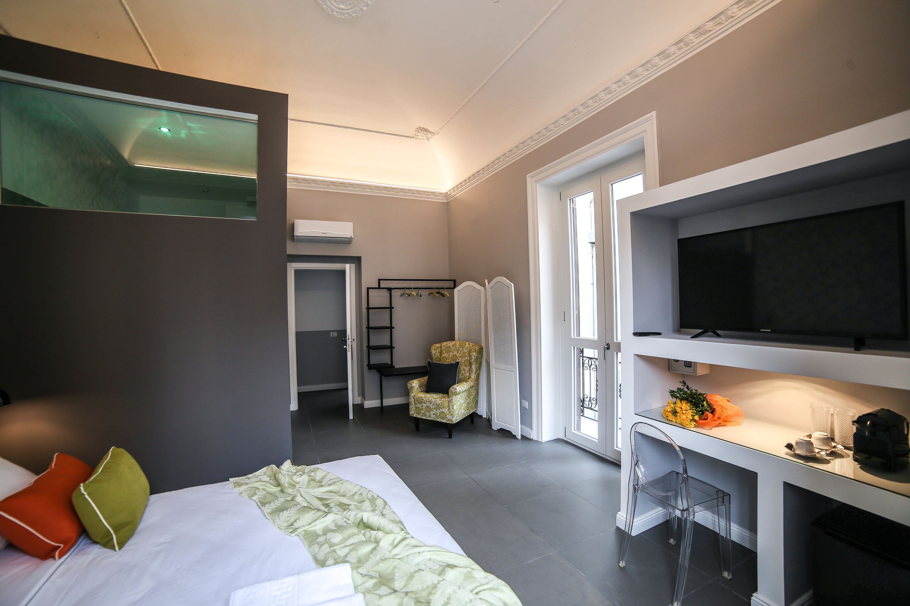 Habitación de hotel moderna con una cama, un escritorio con televisor, una silla y un pequeño balcón.