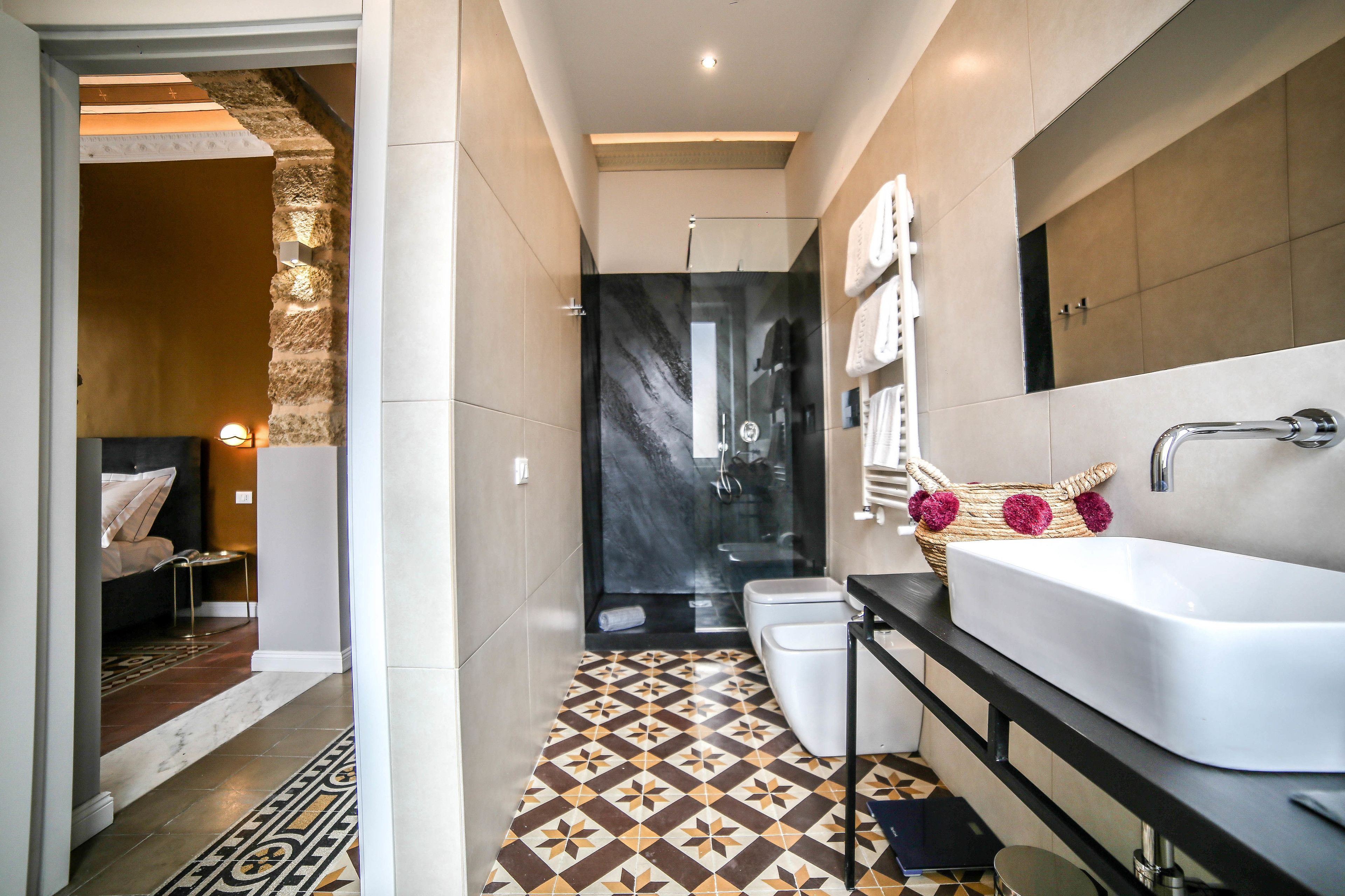 A modern bathroom with a large white sink, a glass shower enclosure, and patterned floor tiles.