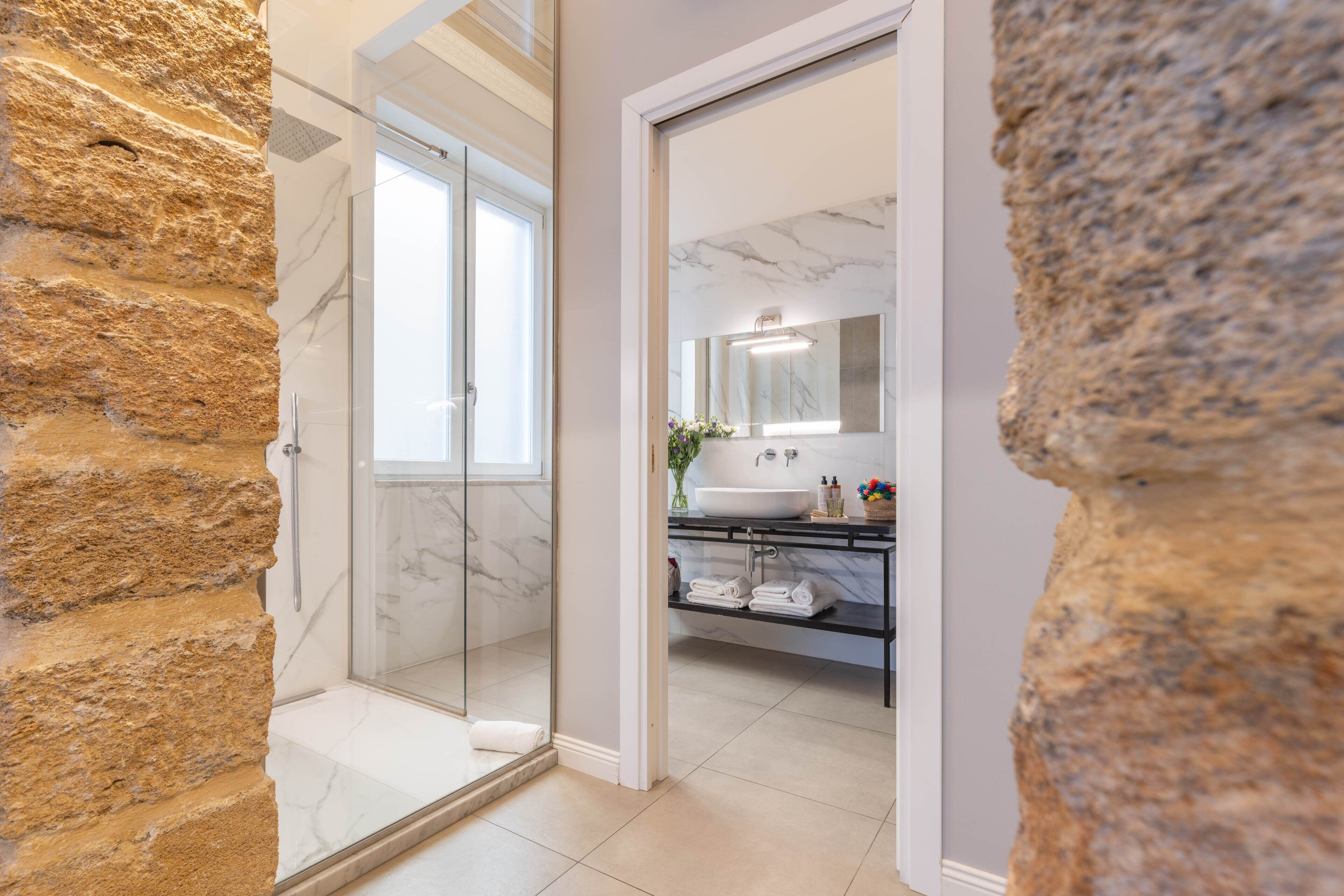 Un bany modern amb dutxa de vidre, parets de marbre i un lavabo amb un gran mirall.