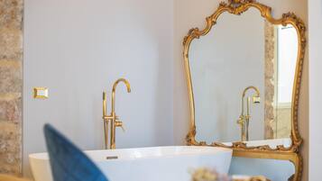 Un baño con una bañera blanca, grifos dorados y un espejo grande y ornamentado.