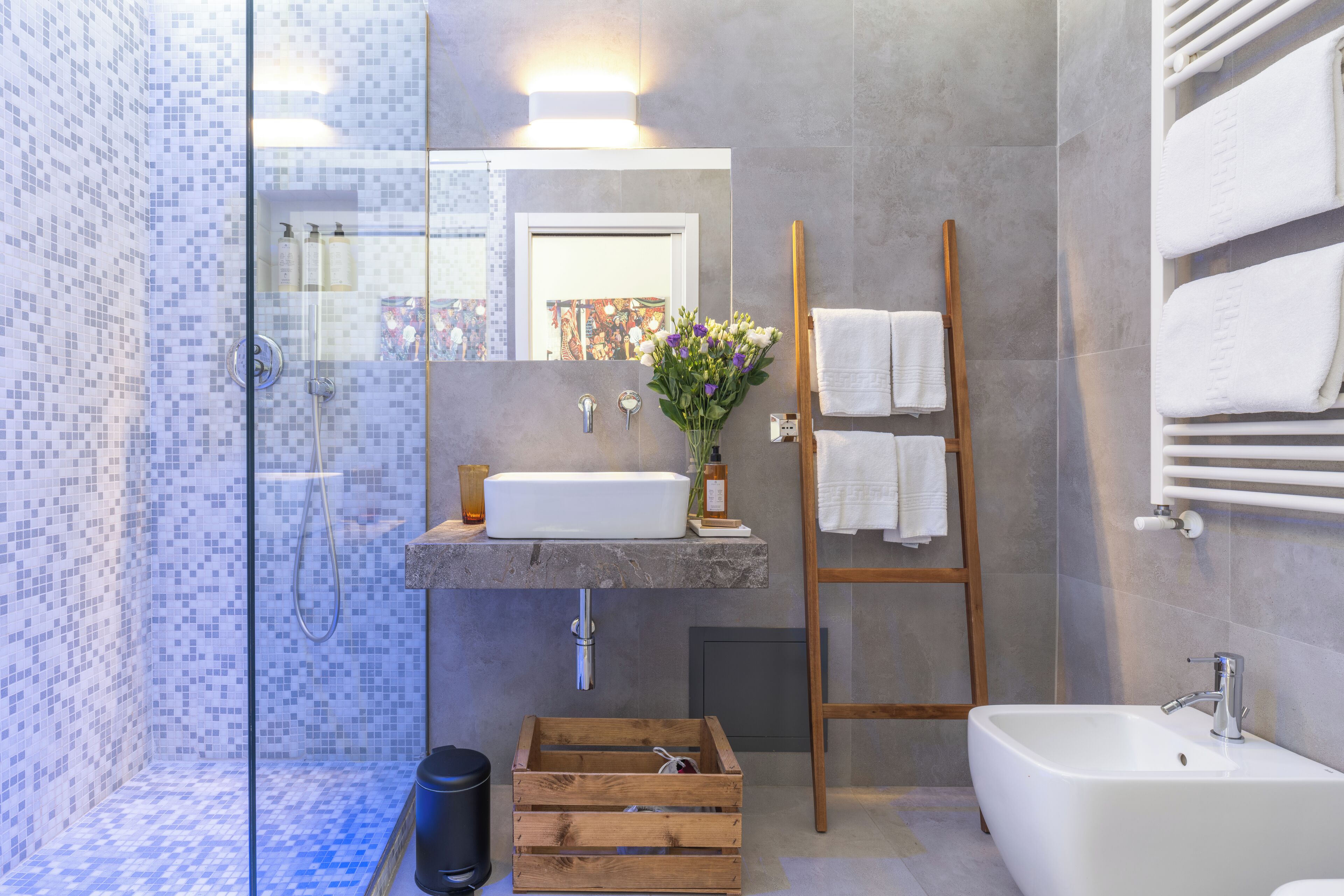 Un baño moderno con ducha de vidrio, una escalera de madera, un lavamanos blanco y un espejo grande.