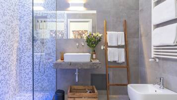 Un baño moderno con ducha de vidrio, una escalera de madera, un lavamanos blanco y un espejo grande.