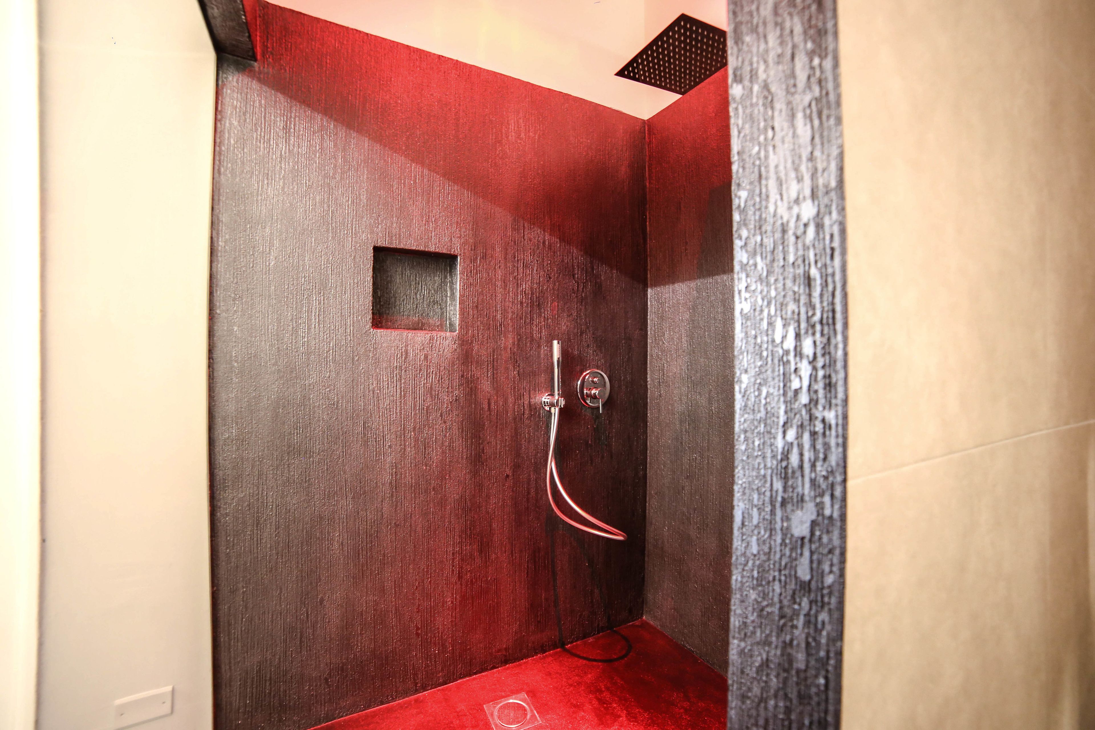 A small, modern shower with a wooden wall and a red floor.