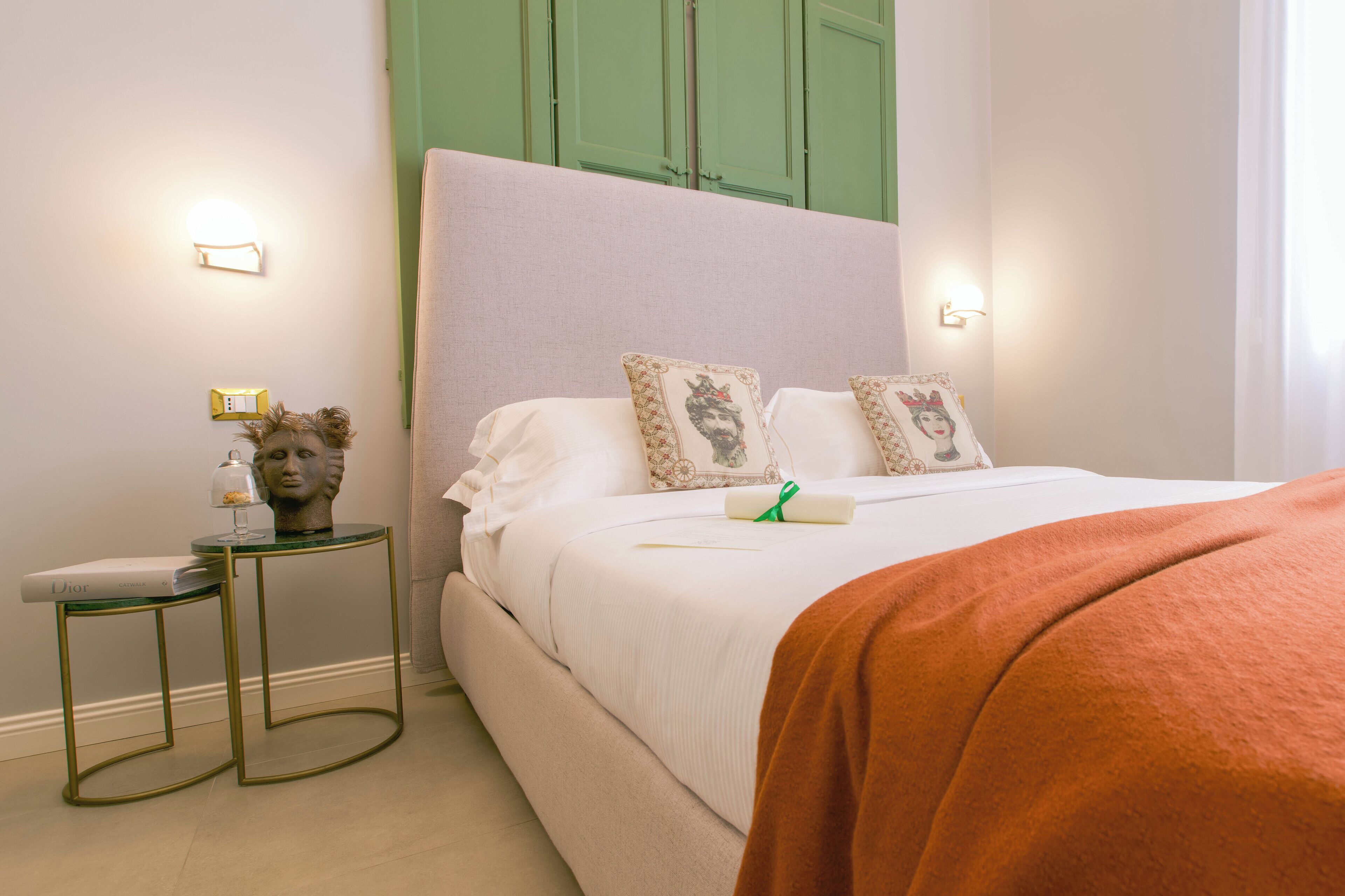 Una cama bien hecha con almohadas, una mesita de noche con lámpara y una pared verde.
