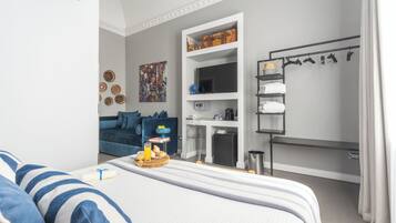 A modern bedroom with a bed, a small kitchenette, a wardrobe, and a seating area with a sofa.
