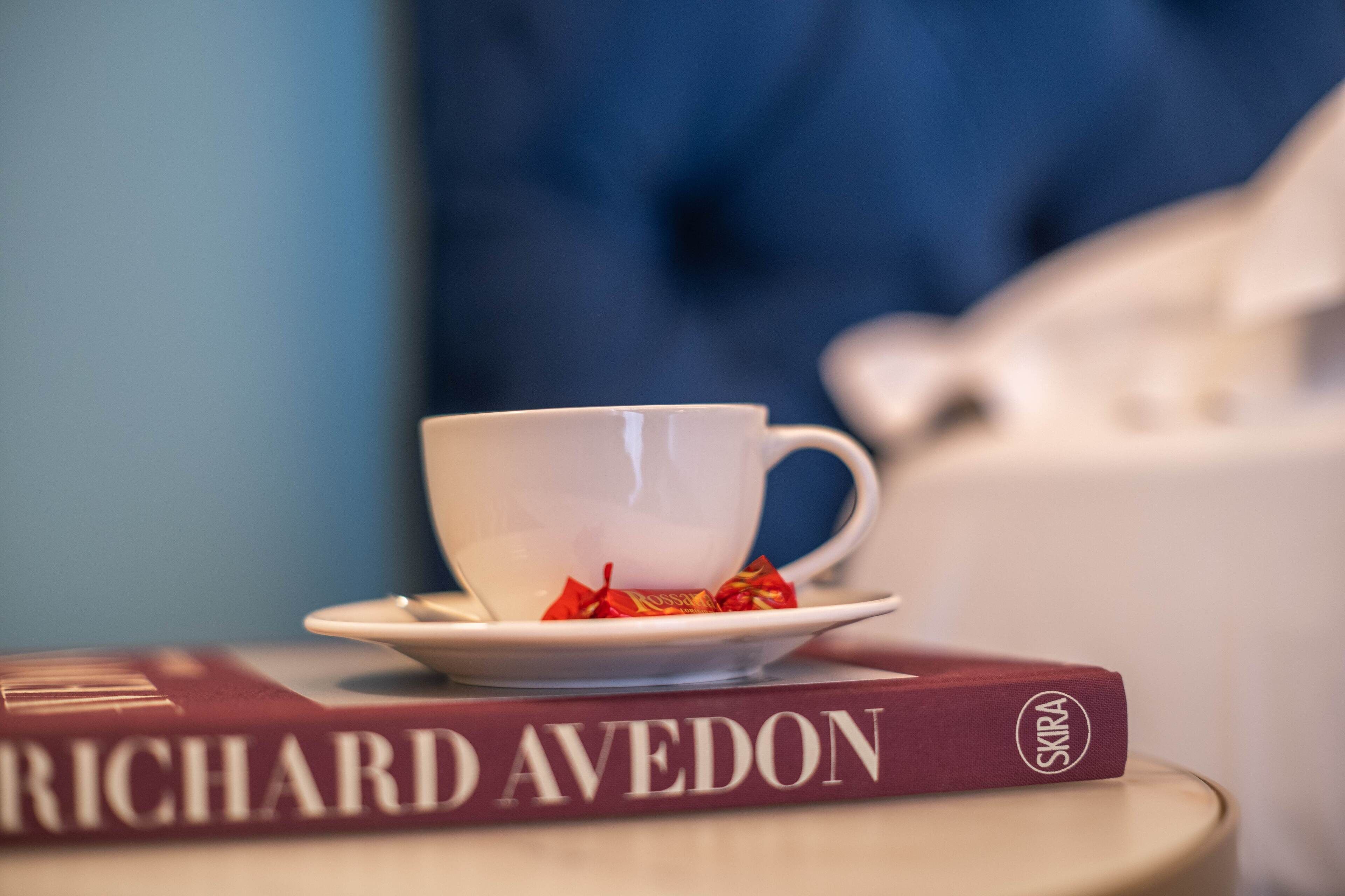 A white cup on a saucer with a red book titled "Richard Avedon" beside it.