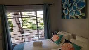 Quarto de hotel com duas camas, janela com persianas, pintura de flores azuis e vista para o verde lá fora.