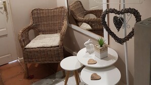 Um quarto com uma cadeira de vime, uma pequena mesa redonda com superfície branca e um espelho na parede.