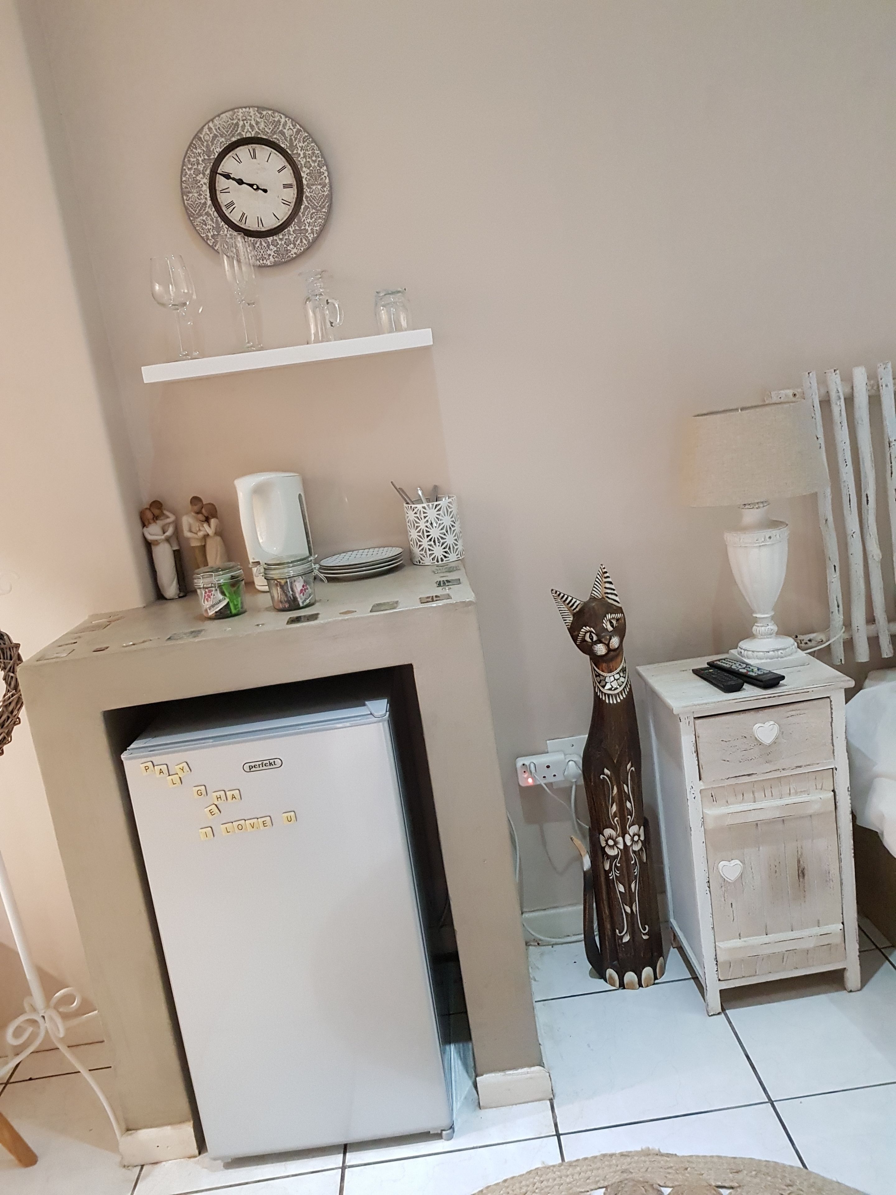 A compact living space with a refrigerator, a clock, a small table with a lamp, and a decorative item.