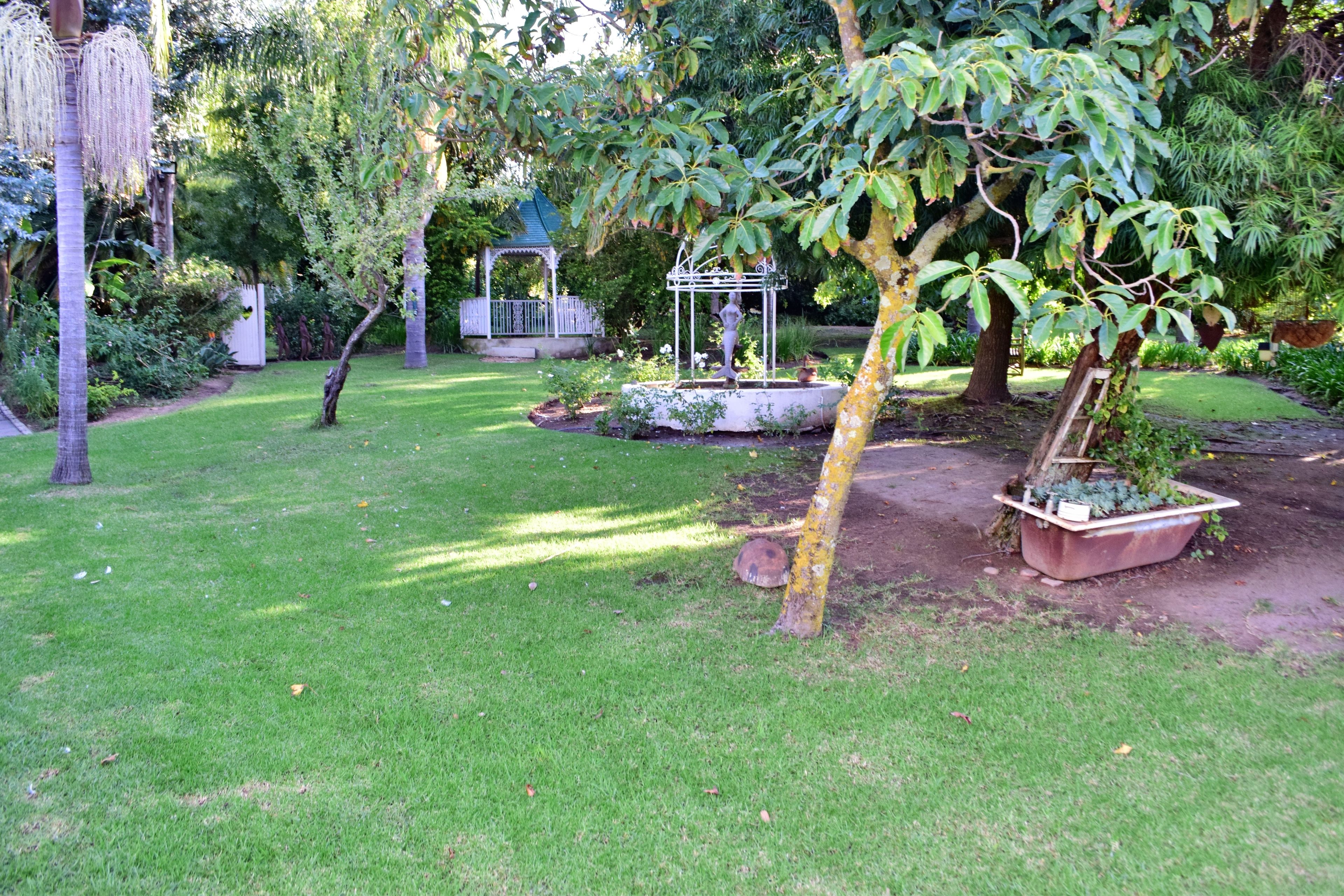 Un jardín bien cuidado con un pabellón, una fuente y diversas plantas.