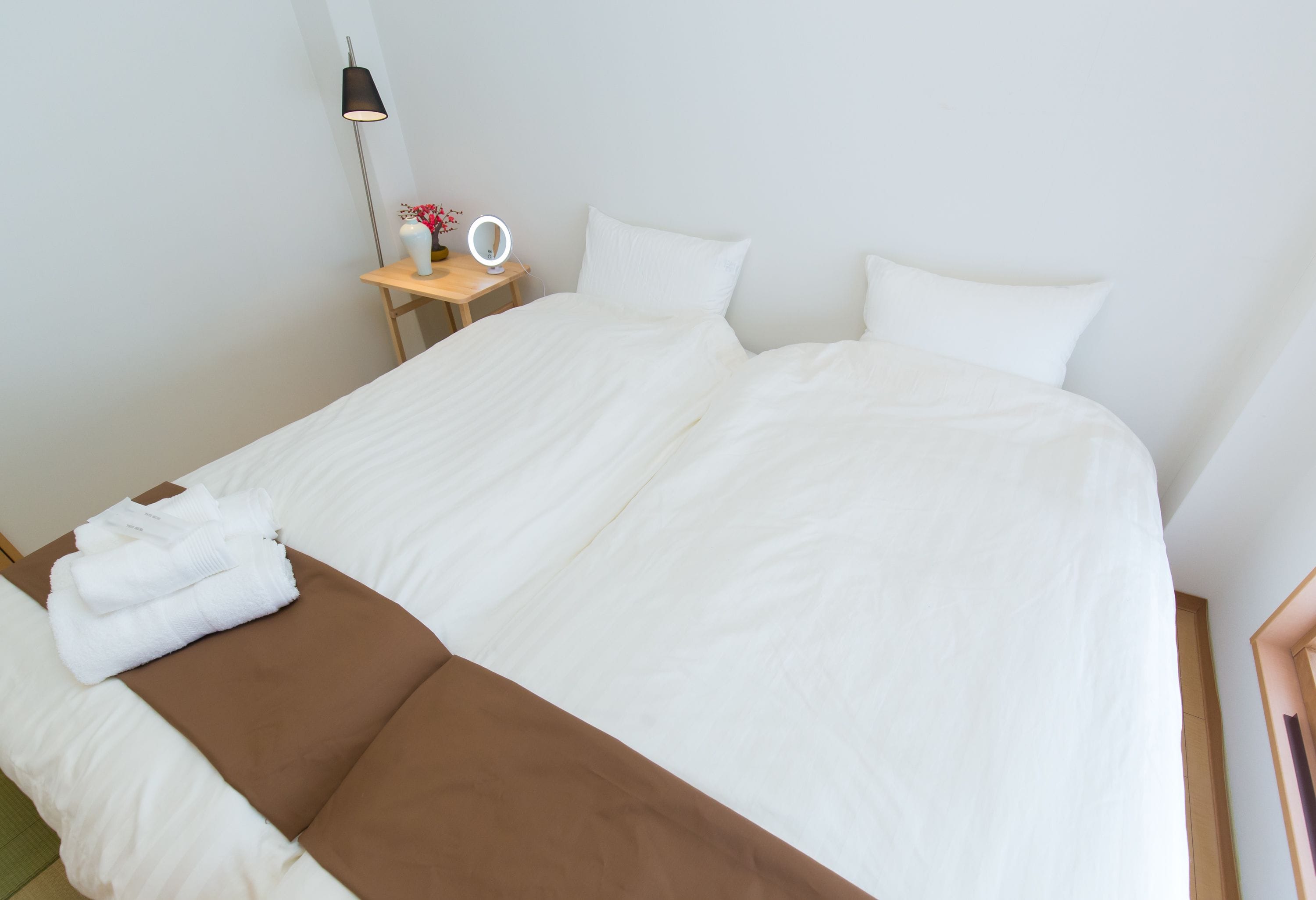 A neatly made bed with white and brown bedding, a bedside table with a lamp, and a mirror.