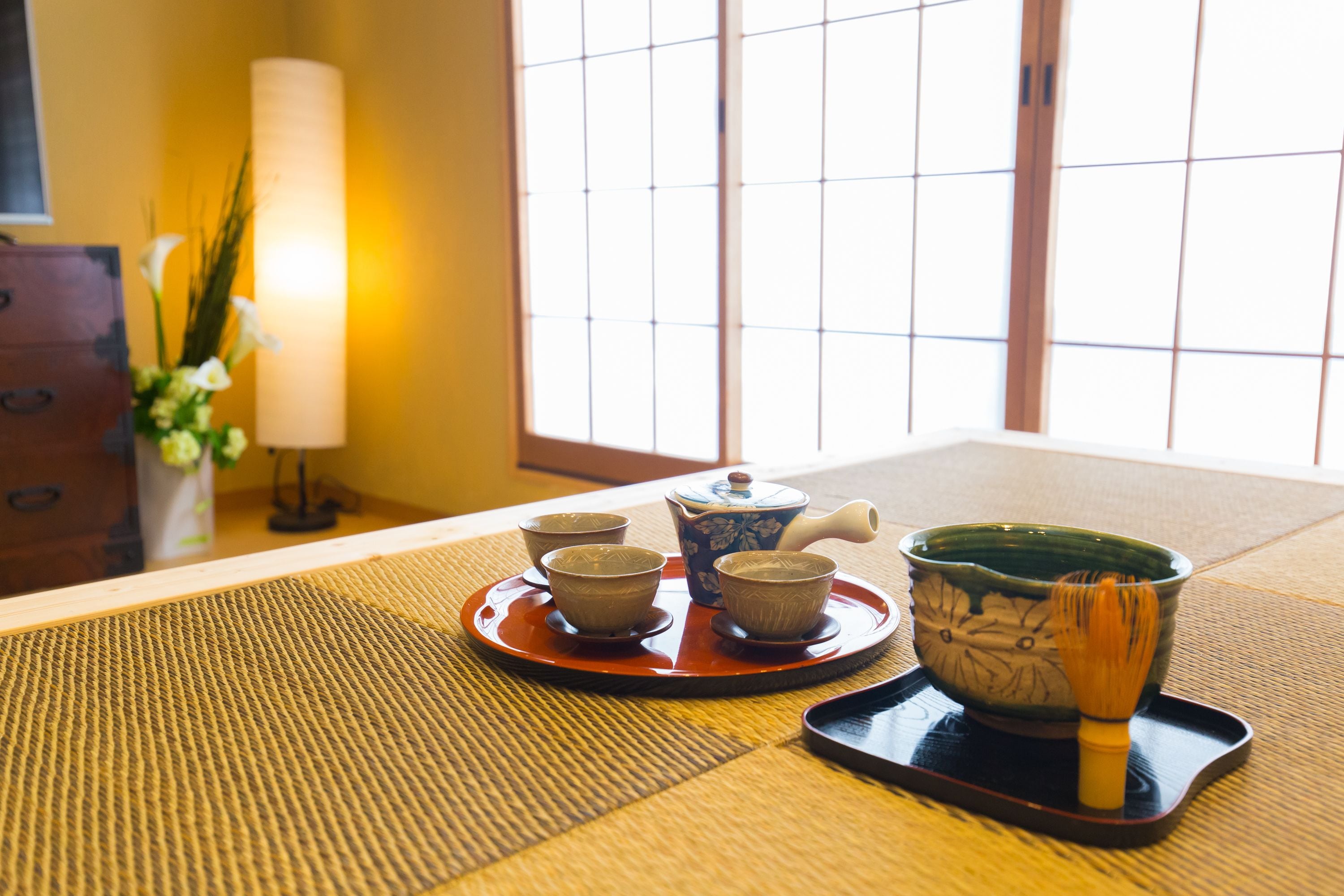 Un service à thé japonais traditionnel est disposé sur un tatami, avec une table en bois et une porte coulissante en arrière-plan.