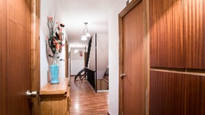 A hallway with wooden flooring, a wooden cabinet with a vase of flowers, and a closed wooden door. - Hostal del Campo (Arévalo)