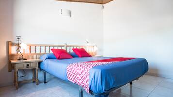 Un lit simple avec une tête de lit en bois, une table de chevet avec une lampe et une couverture à motifs rouges et blancs.