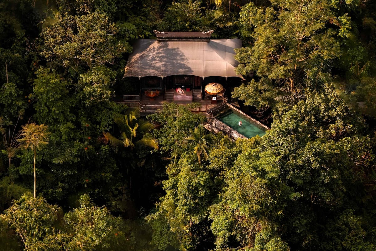 Eine Luftaufnahme zeigt einen abgelegenen Urlaubsort mit einem großen Pool, umgeben von üppiger tropischer Vegetation.
