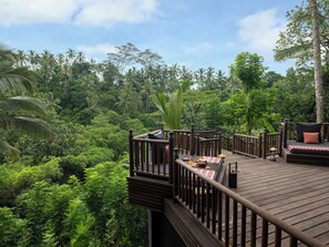 A wooden deck with a checkered tablecloth, surrounded by lush greenery and palm trees. - Capella Ubud, Bali (Tegallalang)
