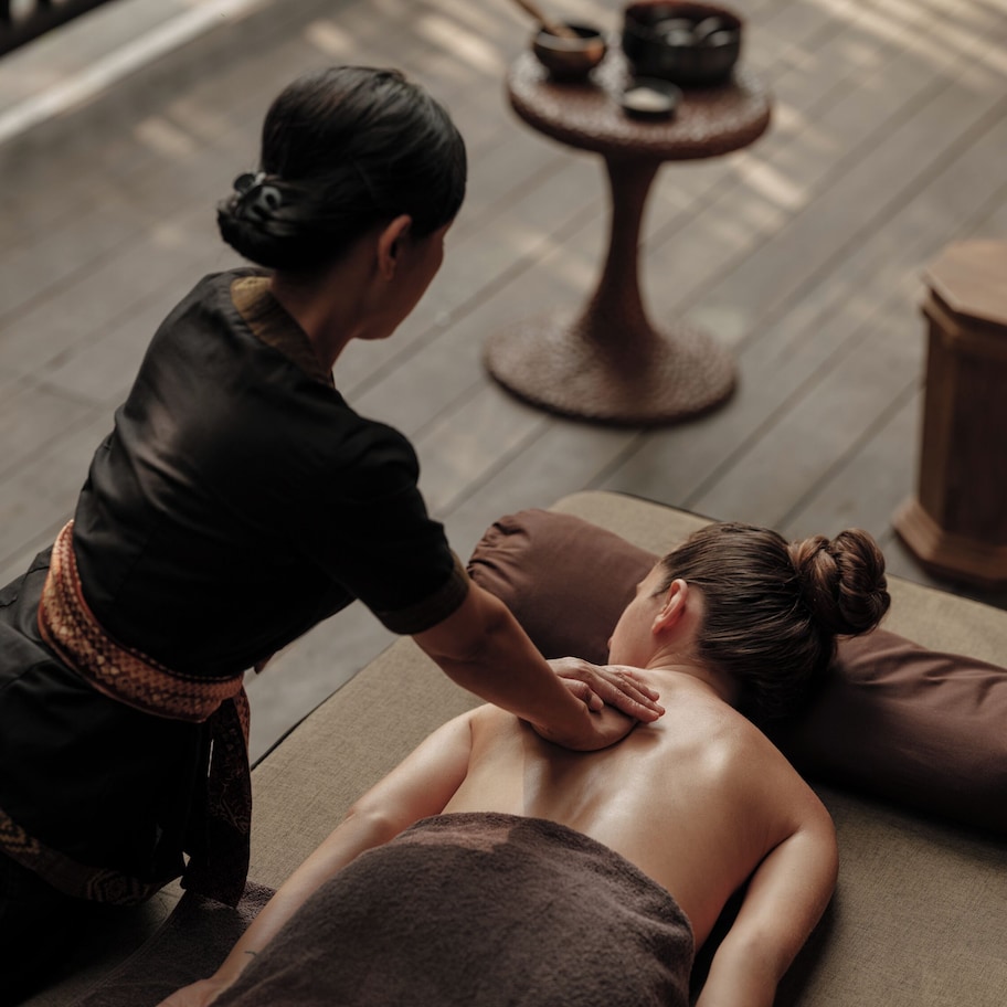 A massage therapy session in a room with a wooden floor, a massage table, and a small round table with bowls and spoons.