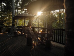 A wooden deck with a table and chairs, surrounded by a railing, and a thatched umbrella providing shade. - Capella Ubud, Bali (Tegallalang)