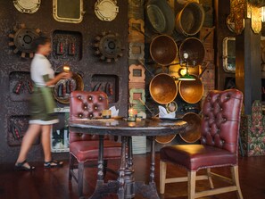 A dining area with a round table, two red upholstered chairs, and a woman serving.