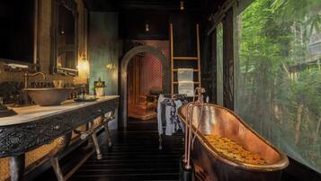 A bathroom with a large copper bathtub, a sink with ornate details, and a mirror.