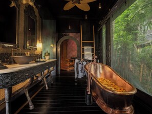 A bathroom with a large copper bathtub, a sink with ornate details, and a mirror.