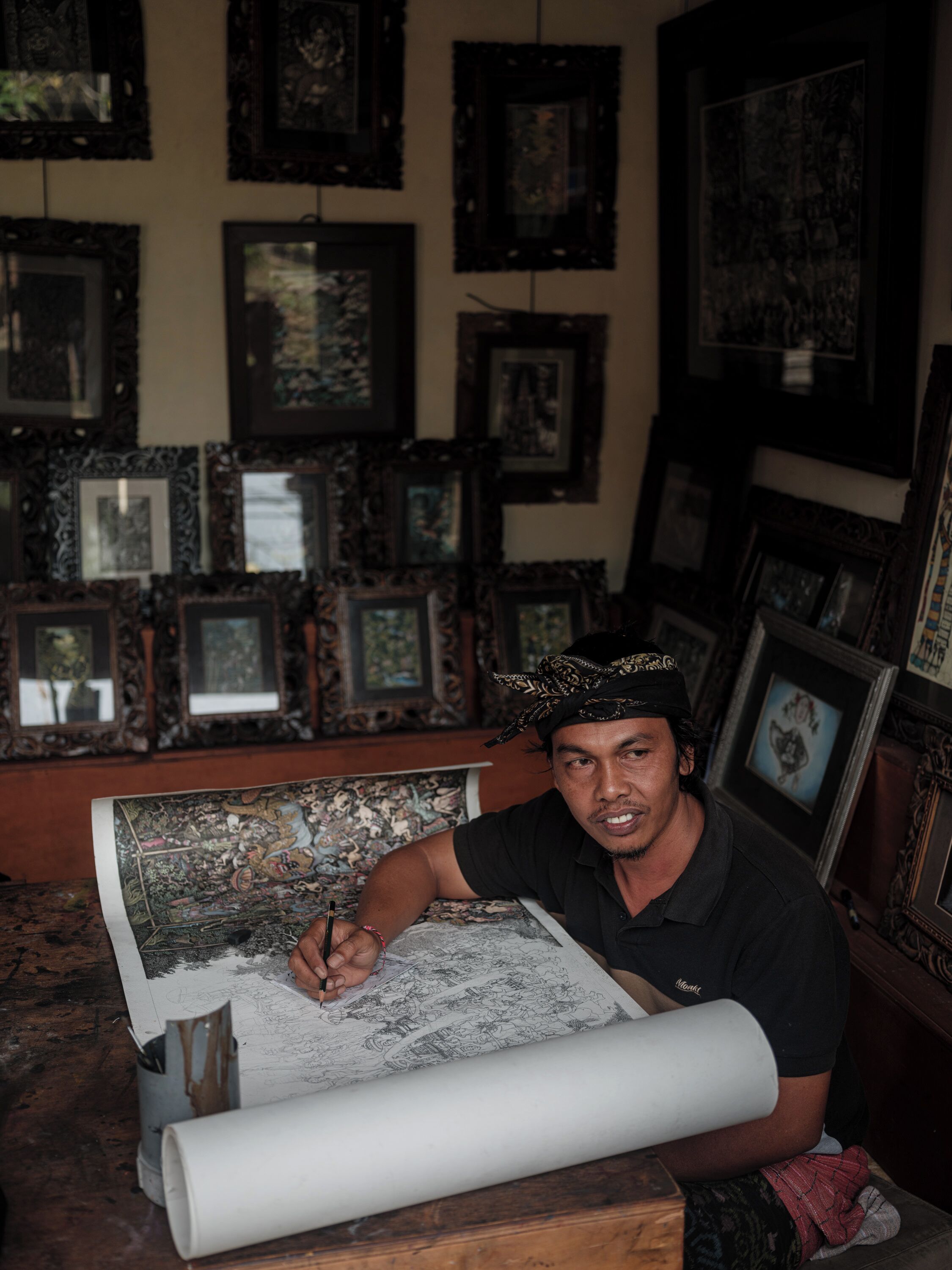 A person drawing on a large sheet of paper in a room with many framed pictures on the walls.